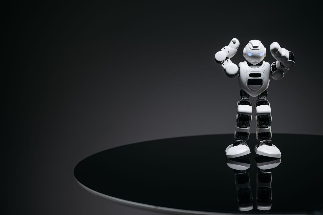 About A small humanoid robot with glowing eyes on a reflective table in a dark setting.